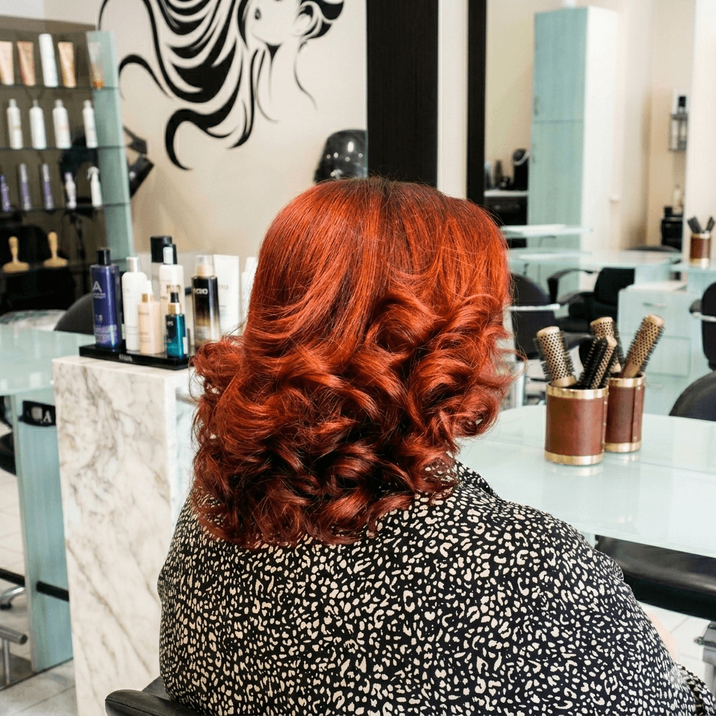 Donna con capelli ricci rosso rame brillante seduta in un salone di bellezza professionale.