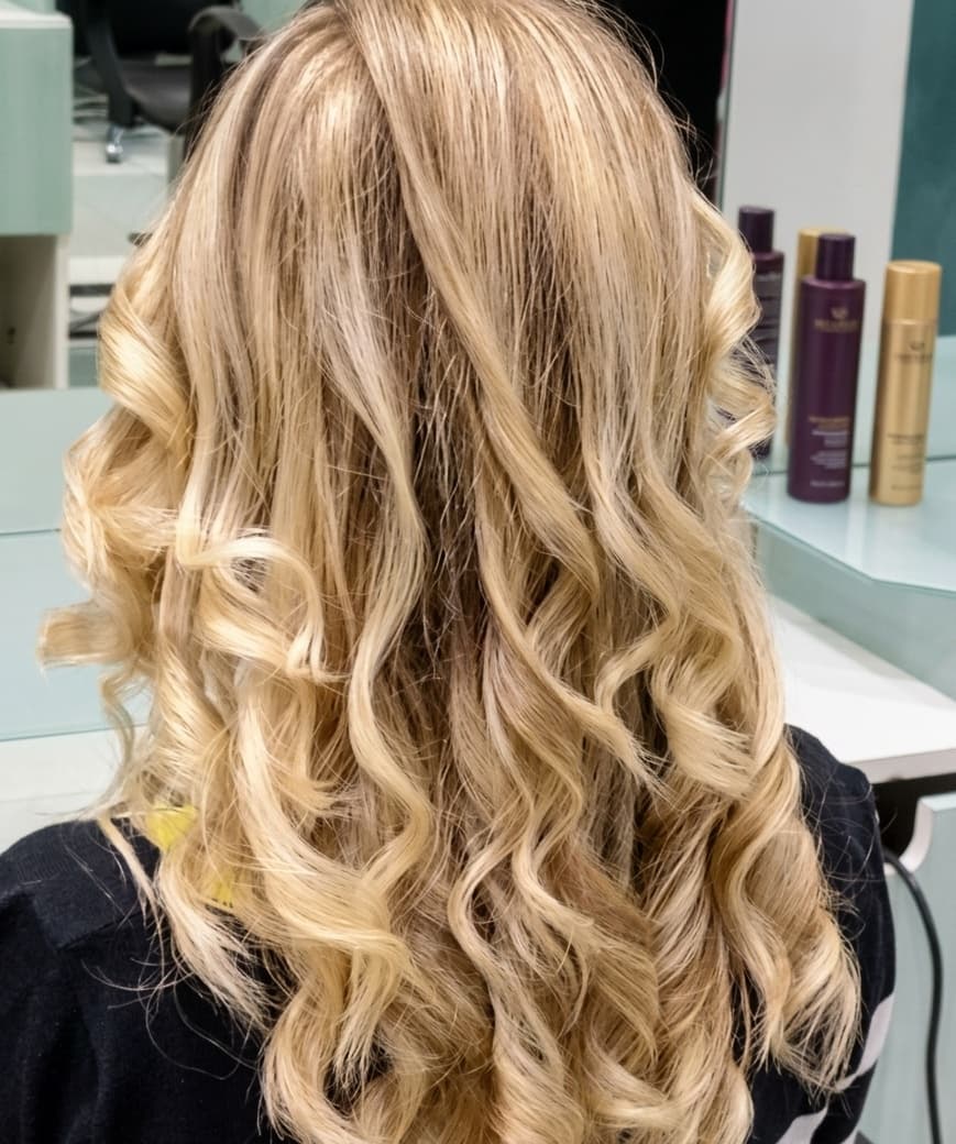 Lunghi capelli biondi con boccoli morbidi e definiti, visti di spalle in un salone.